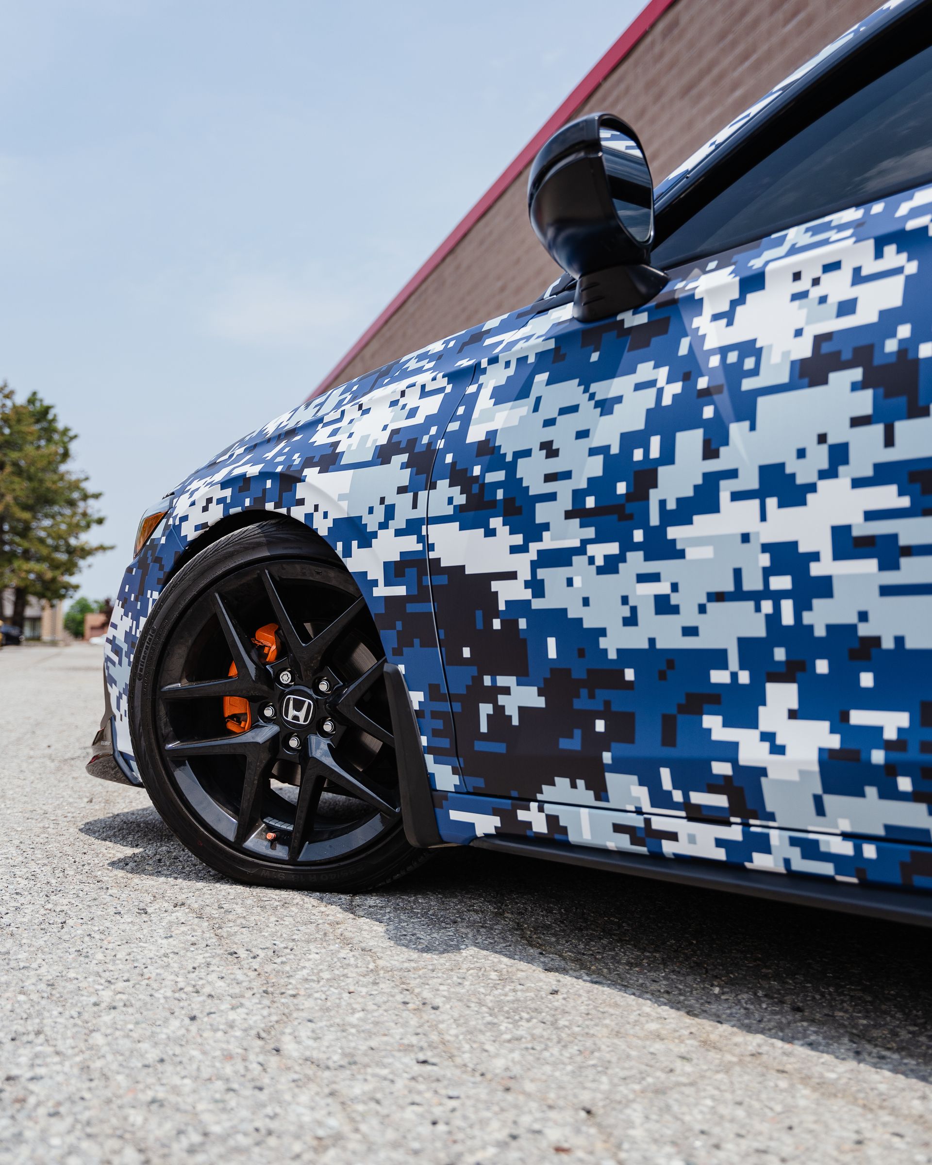 A car with a camouflage wrap is parked in front of a building