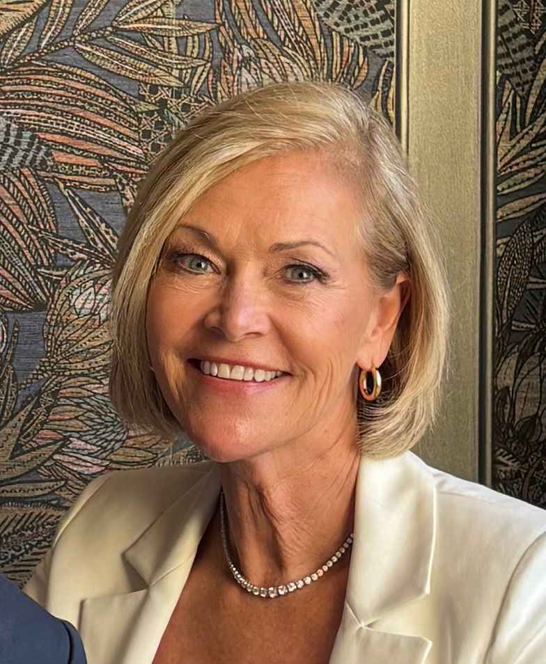 Smiling woman in a coral jacket and patterned top against a white background