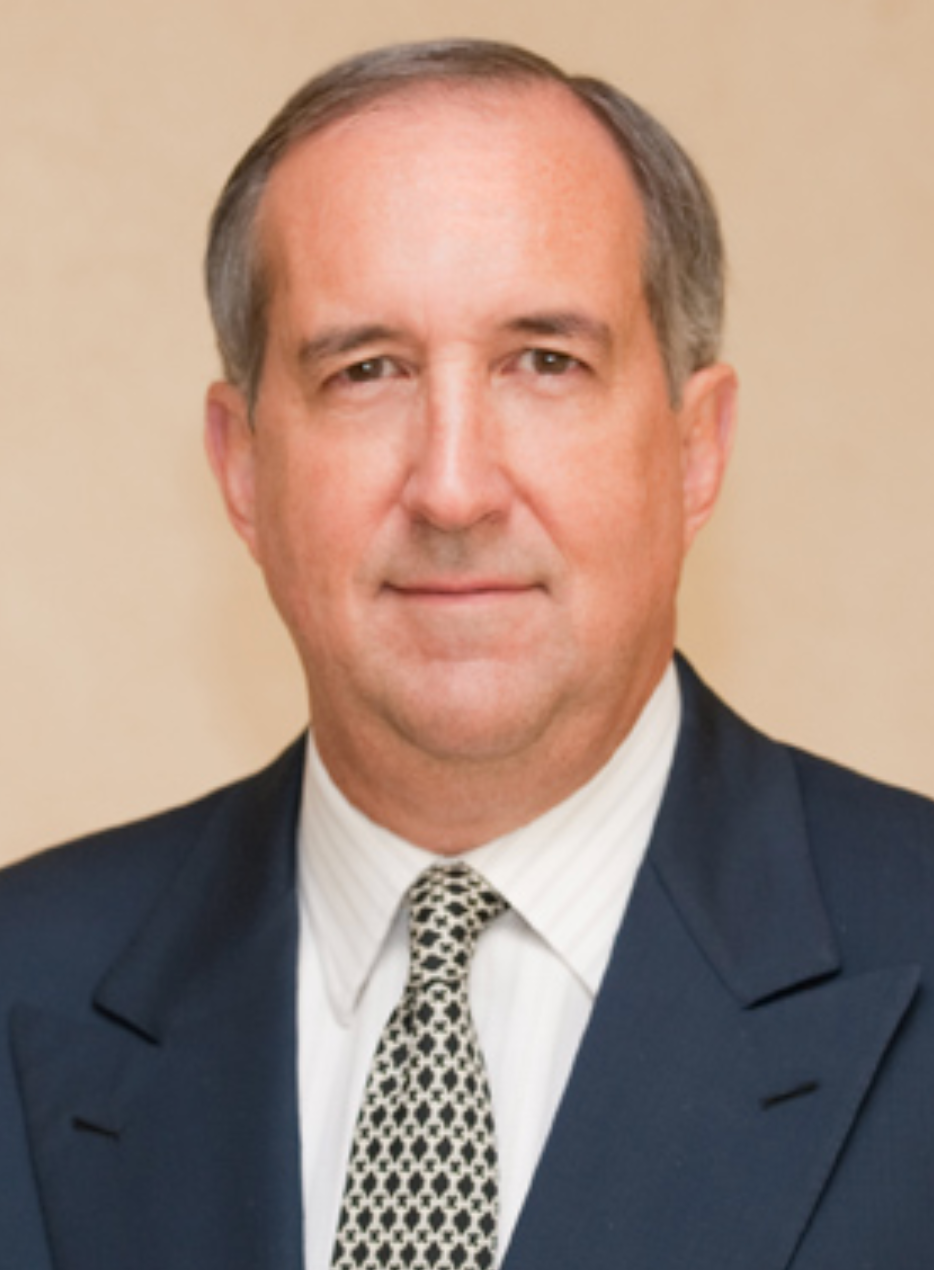 Studio headshot of a man in a dark suit and patterned tie against a beige background