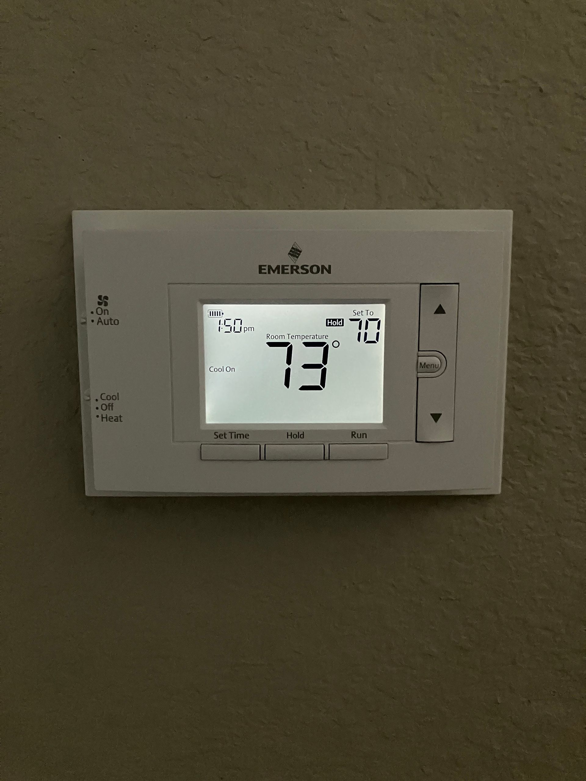 Wall-mounted digital thermostat displaying 73°F on a beige wall.