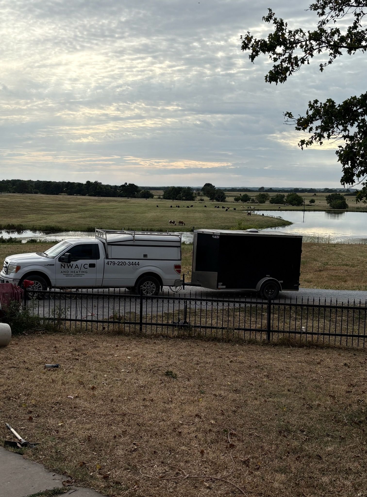 White utility truck and black trailer parked beside a grassy marsh under a cloudy sky.