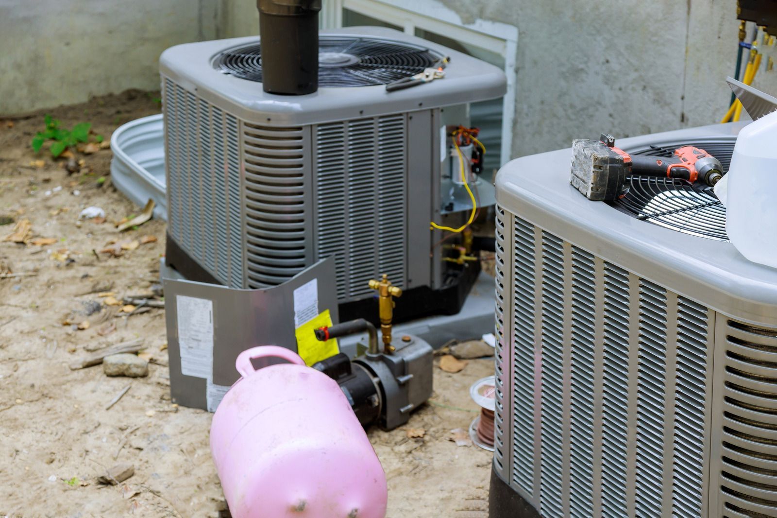 Two outdoor HVAC units with exposed wiring and a pink plastic container in front of them