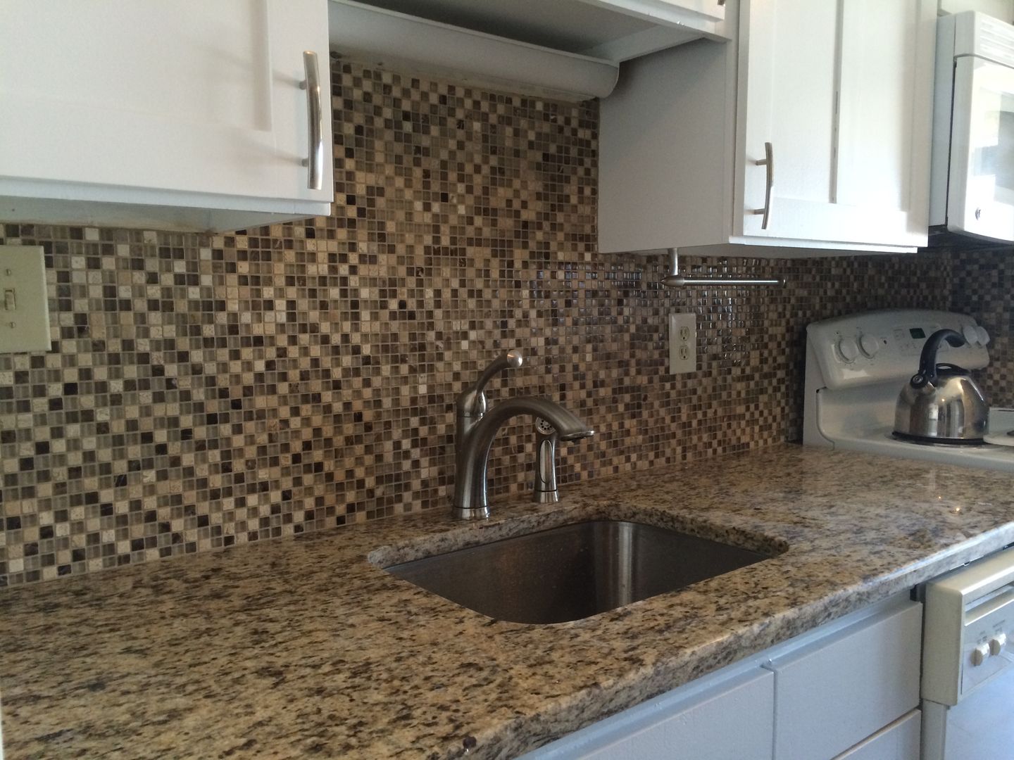 Kitchen with granite countertop, mosaic tile backsplash, stainless steel sink, and white cabinets.