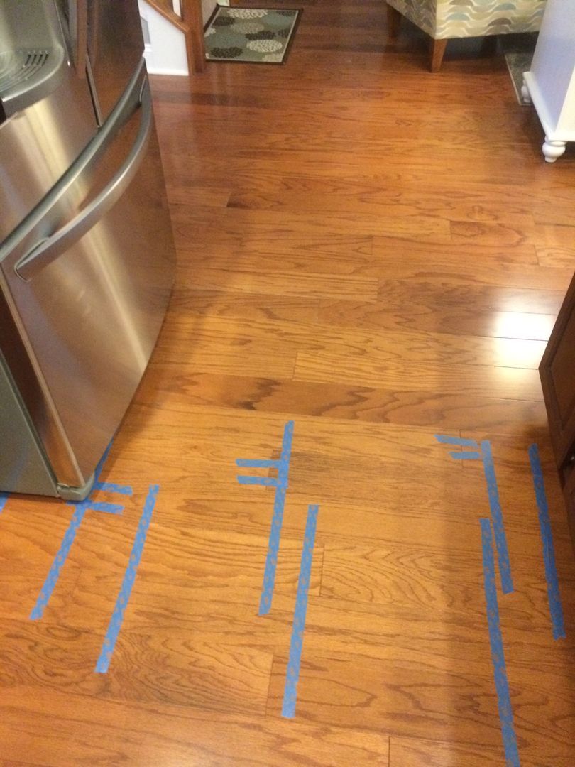Wooden floor with blue painter's tape lines marking locations near a stainless steel refrigerator.