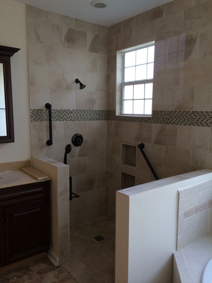 Accessible shower with beige tile, dark fixtures, grab bars, and a window.