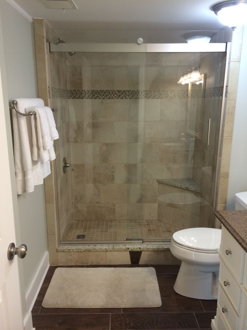 Bathroom with a tiled shower, toilet, and towel rack. Brown floor, beige walls, and white cabinets.