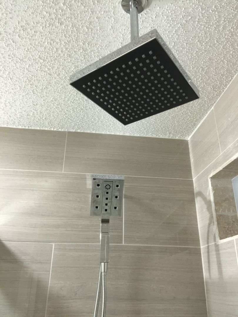 Square rain shower head in a tiled shower with handheld shower.
