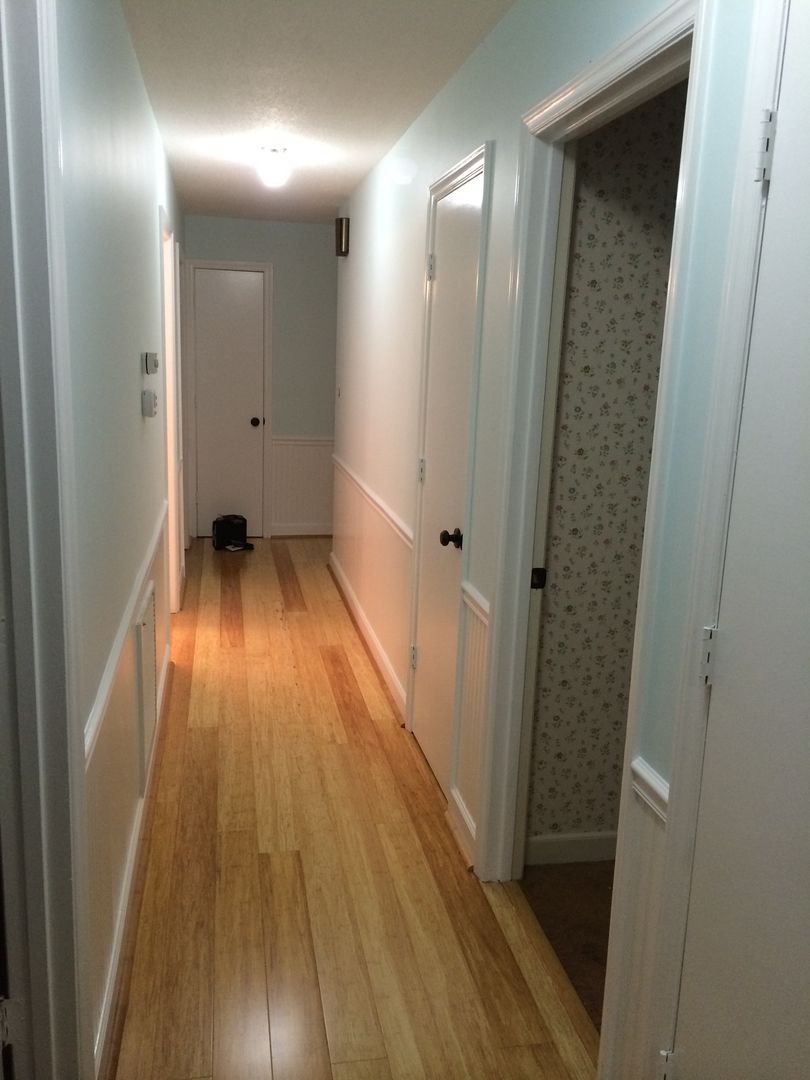 Long hallway with wooden floor and light blue walls, doors on both sides.