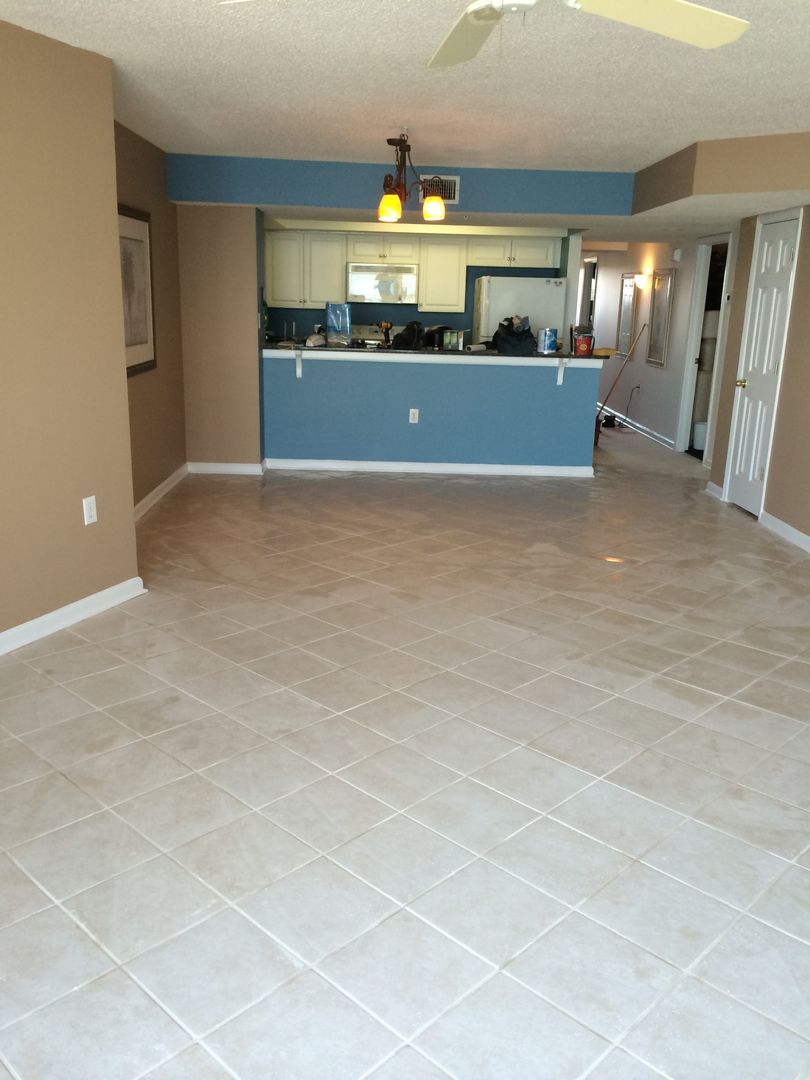 Empty living room with tan tile floor, blue and tan walls, and a view into the kitchen.
