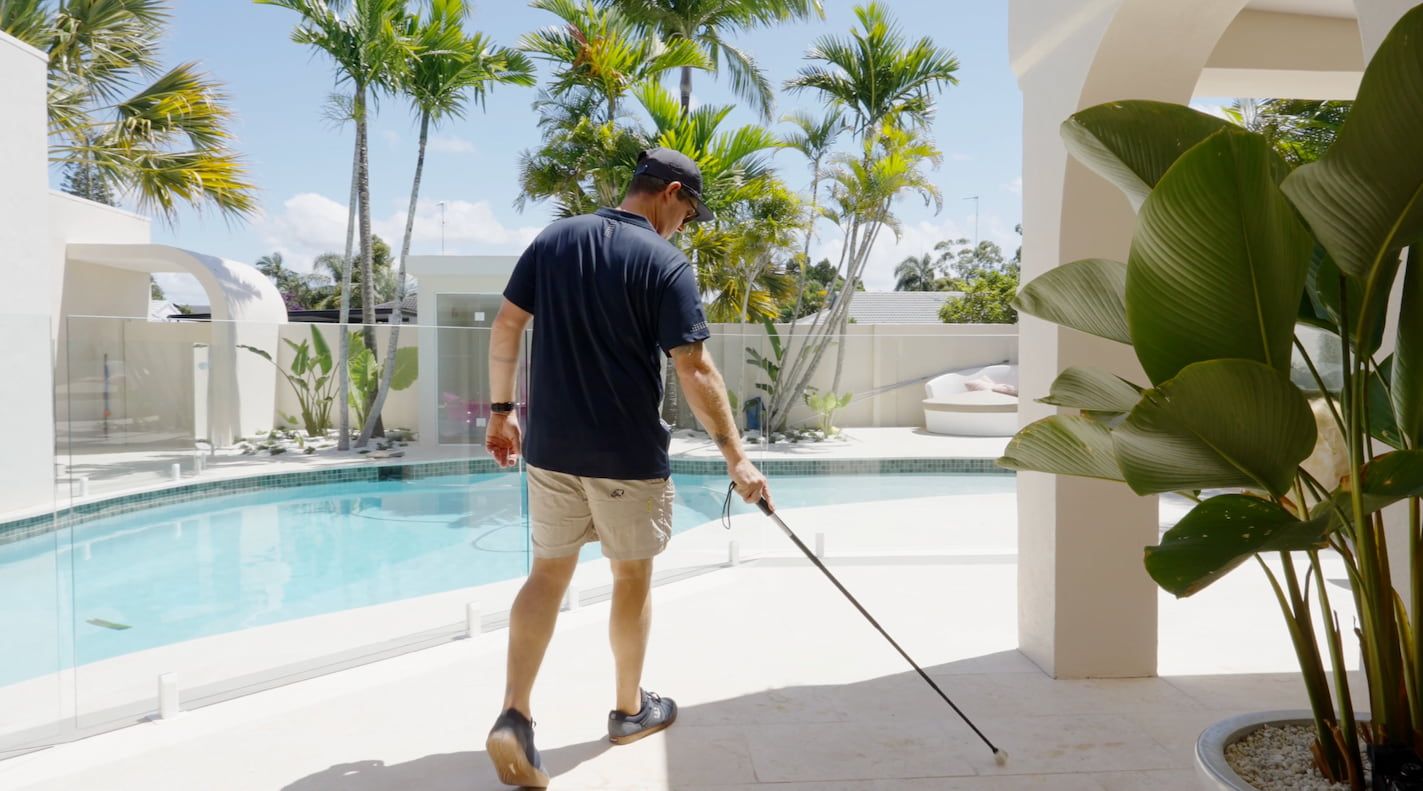 A man is walking across a patio next to a pool.