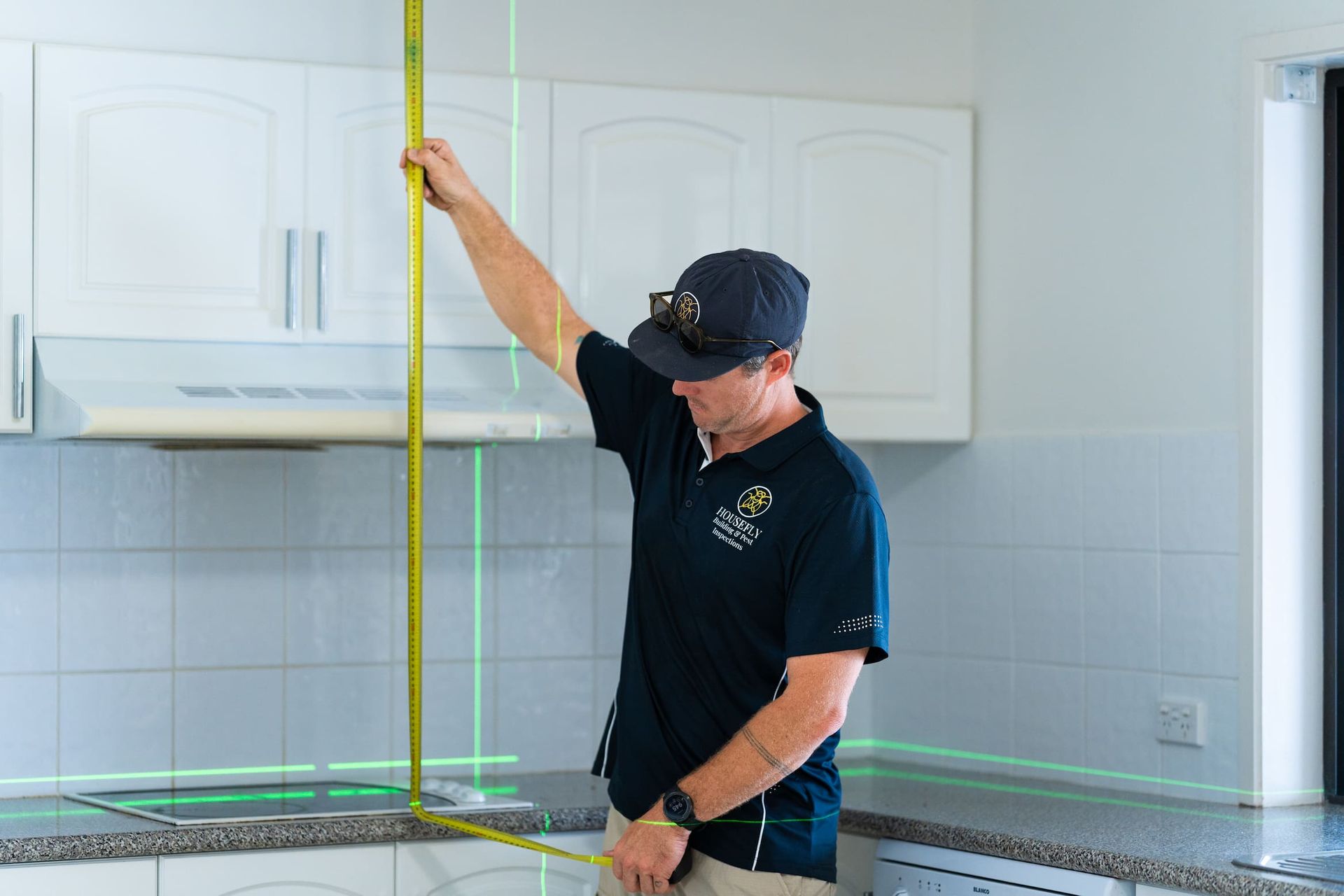 A man is measuring a cabinet with a tape measure in a kitchen.