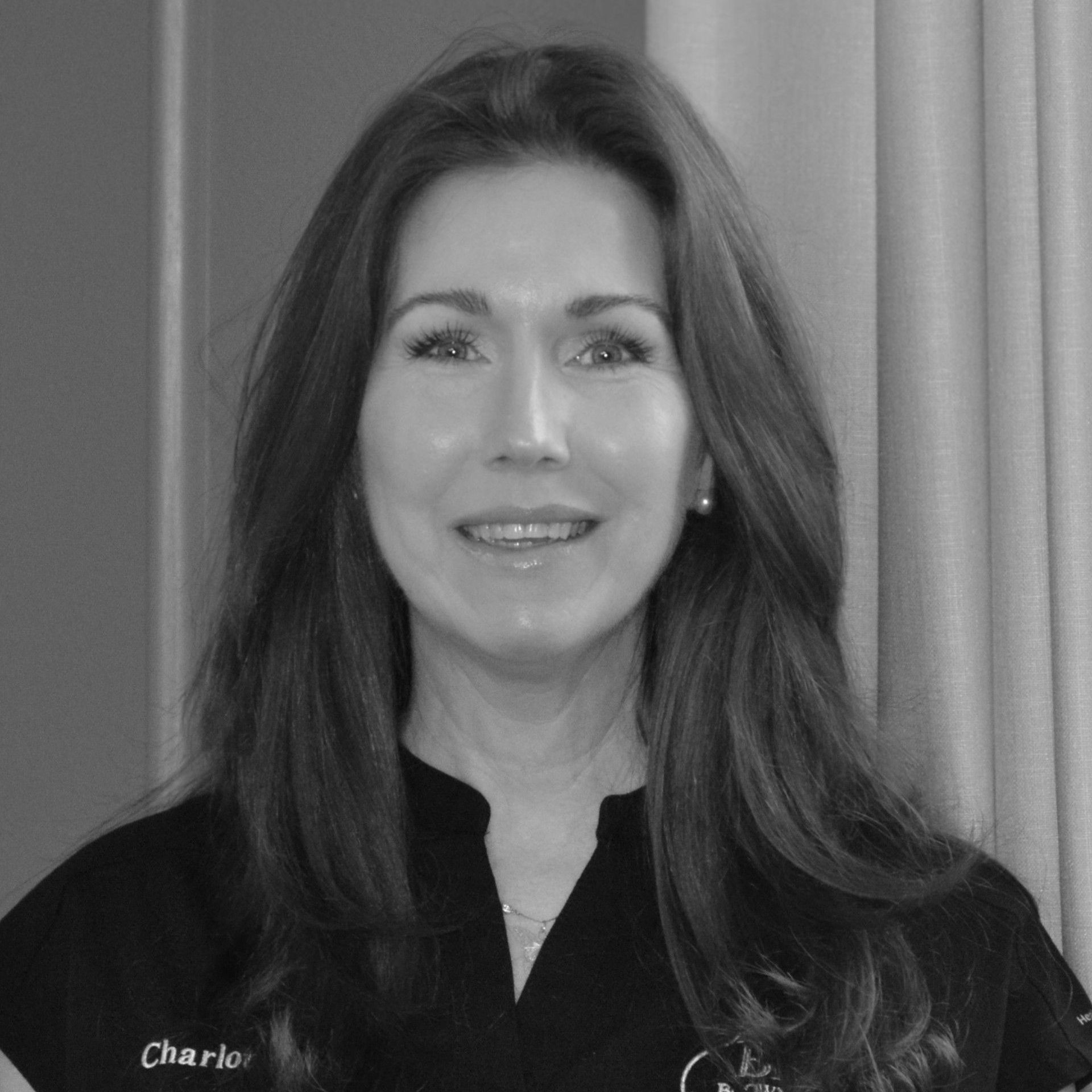 A woman with long hair is wearing a black shirt and smiling in a black and white photo.