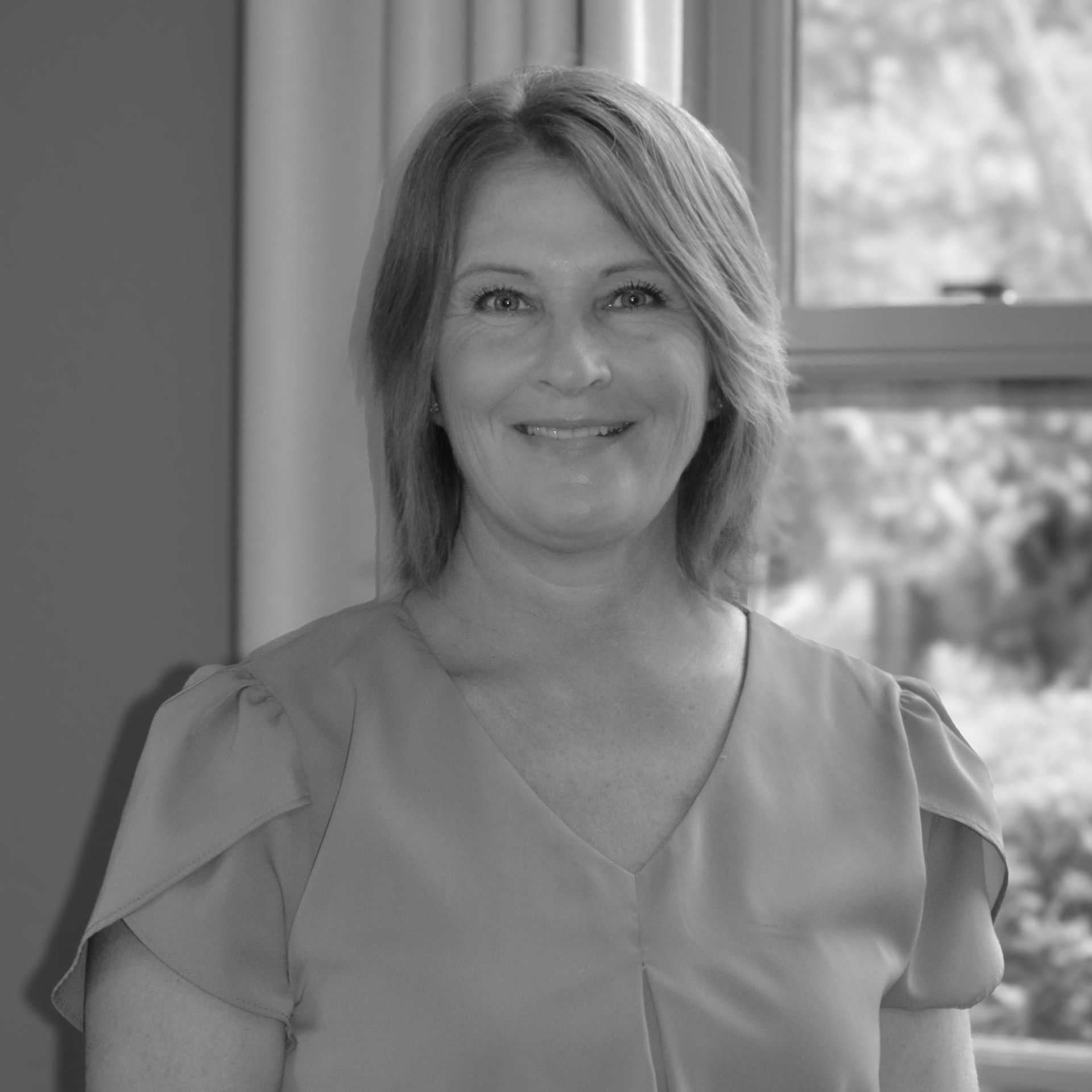A woman is smiling in front of a window in a black and white photo.