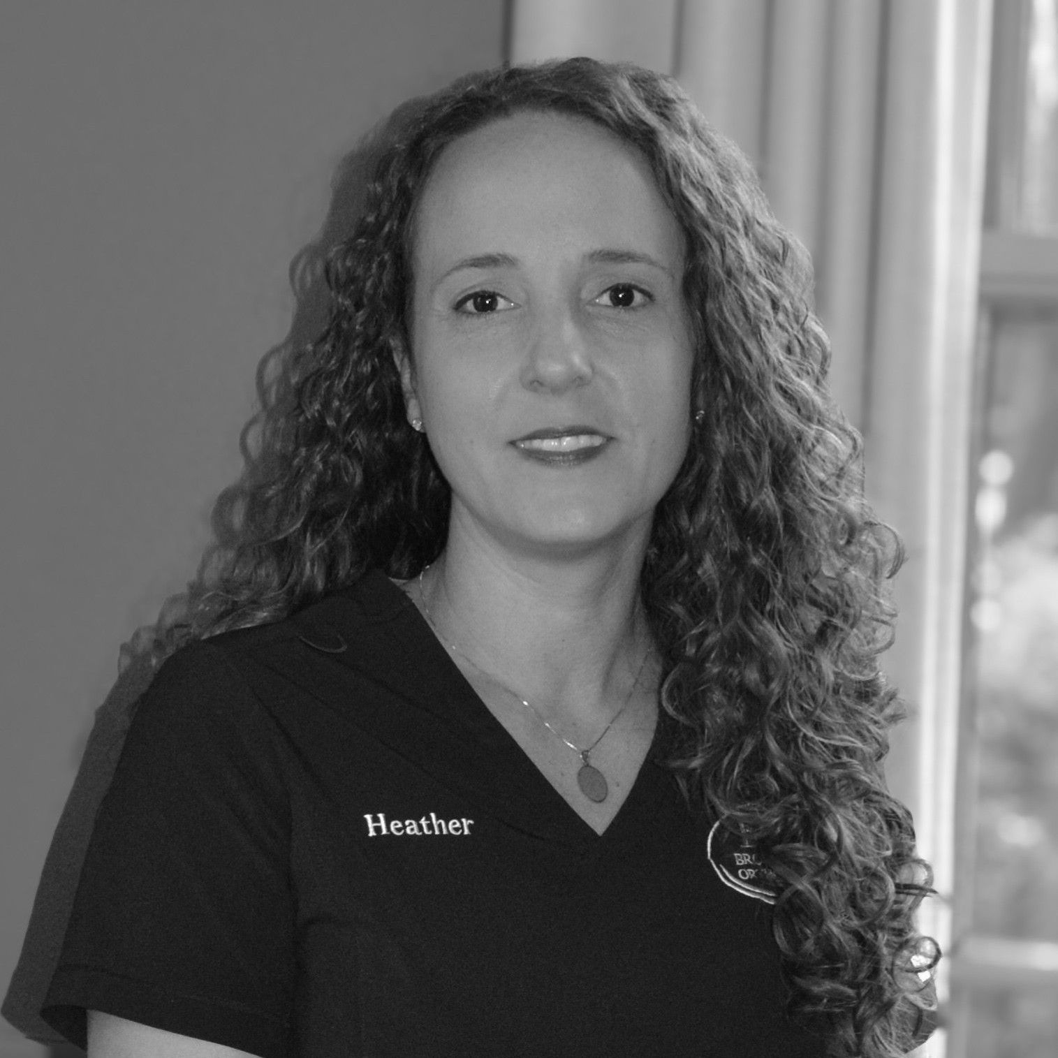 A woman with curly hair is wearing a gray shirt and smiling.
