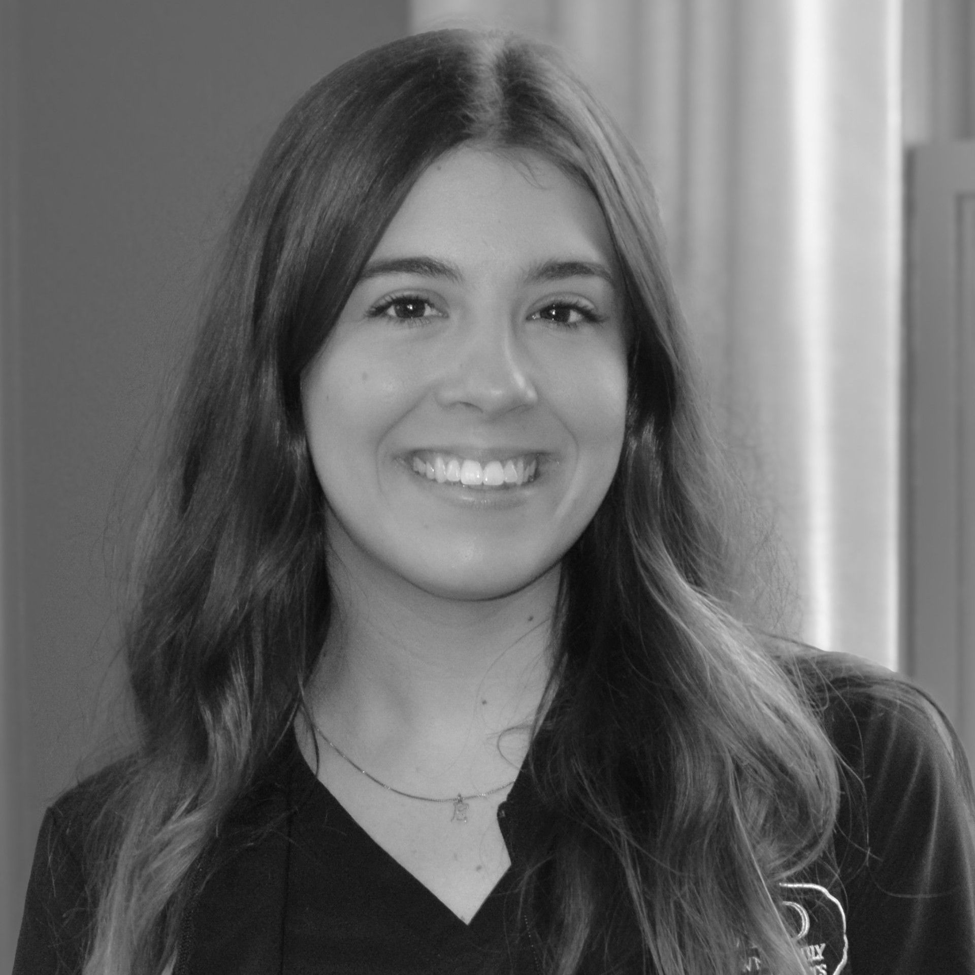 A black and white photo of a smiling woman wearing a scrub top.