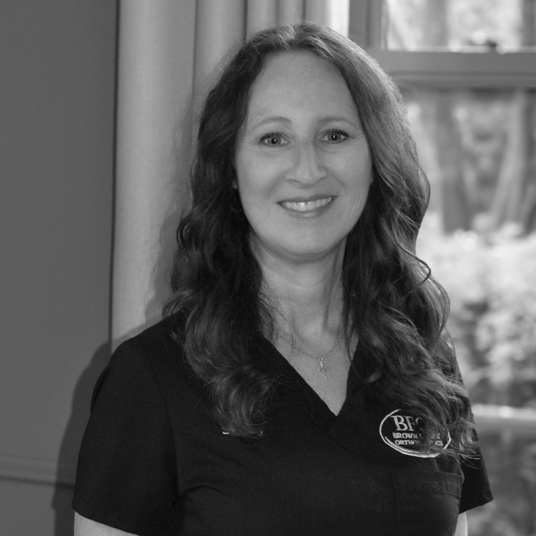 A woman in a black shirt is smiling in front of trees.