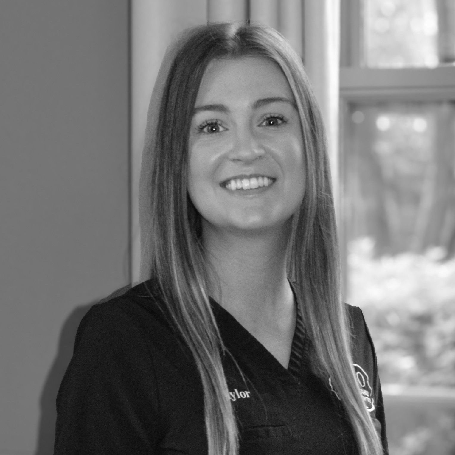 A black and white photo of a smiling woman standing in front of a window.