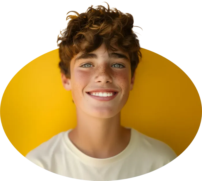 A young boy with curly hair is smiling in front of a yellow background