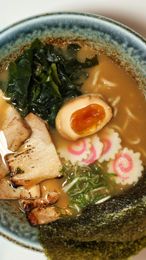 Bowl of ramen with noodles, seaweed, egg, pork slices, and pink fish cake in broth