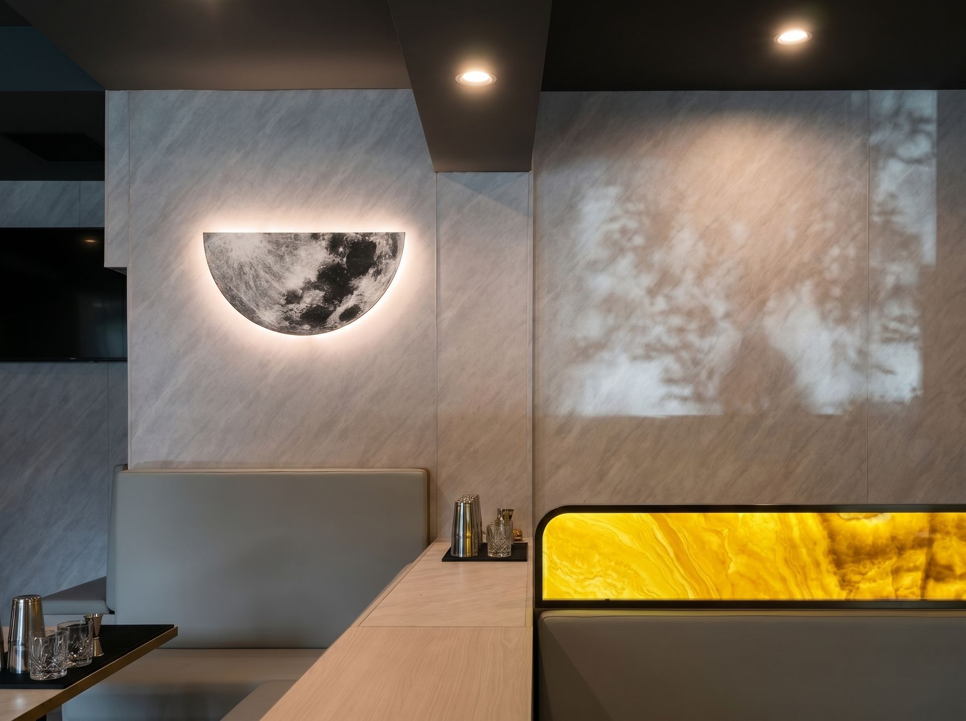 Modern cafe booth with marble wall, warm lighting, and a yellow backlit bench panel.