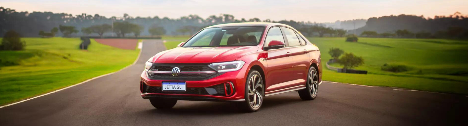 Um Volkswagen Jetta vermelho está dirigindo por uma estrada secundária.