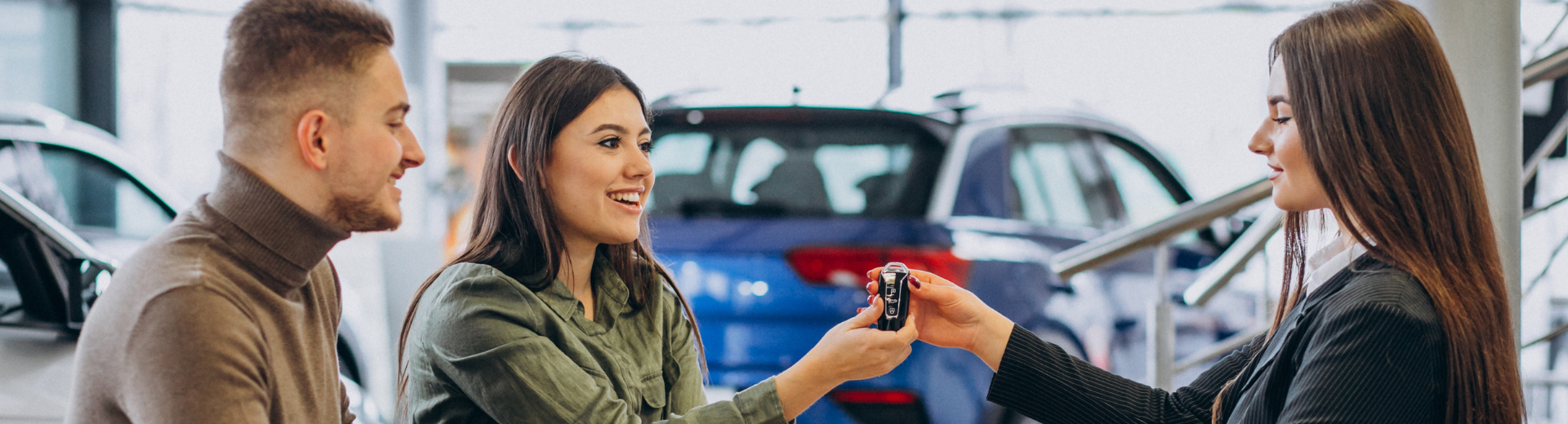 Uma mulher está entregando a chave do carro a um homem e a uma mulher em um showroom de automóveis.