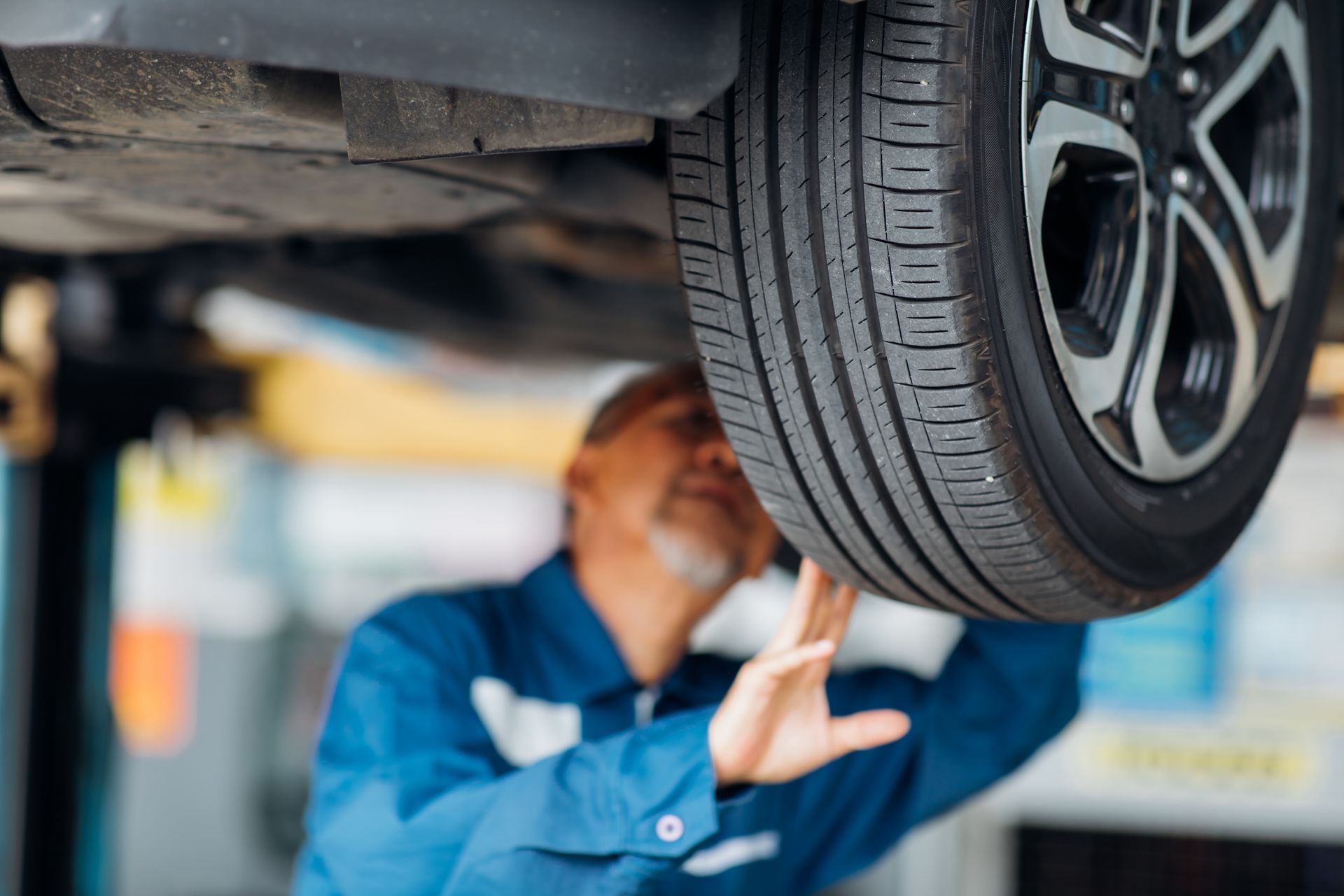 Technician performing car maintenance while inspecting the underside of a vehicle on a lift.