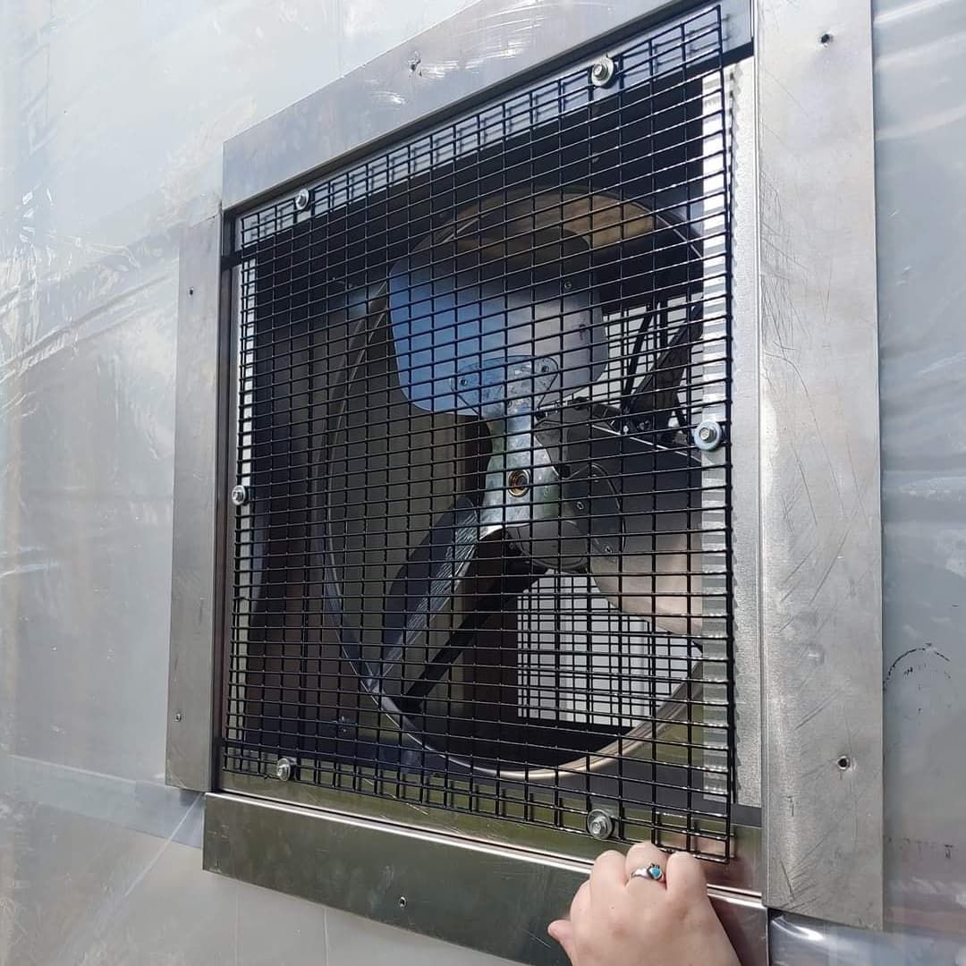 A large ventilation fan covered with a metal grid. Hand reaches toward it.