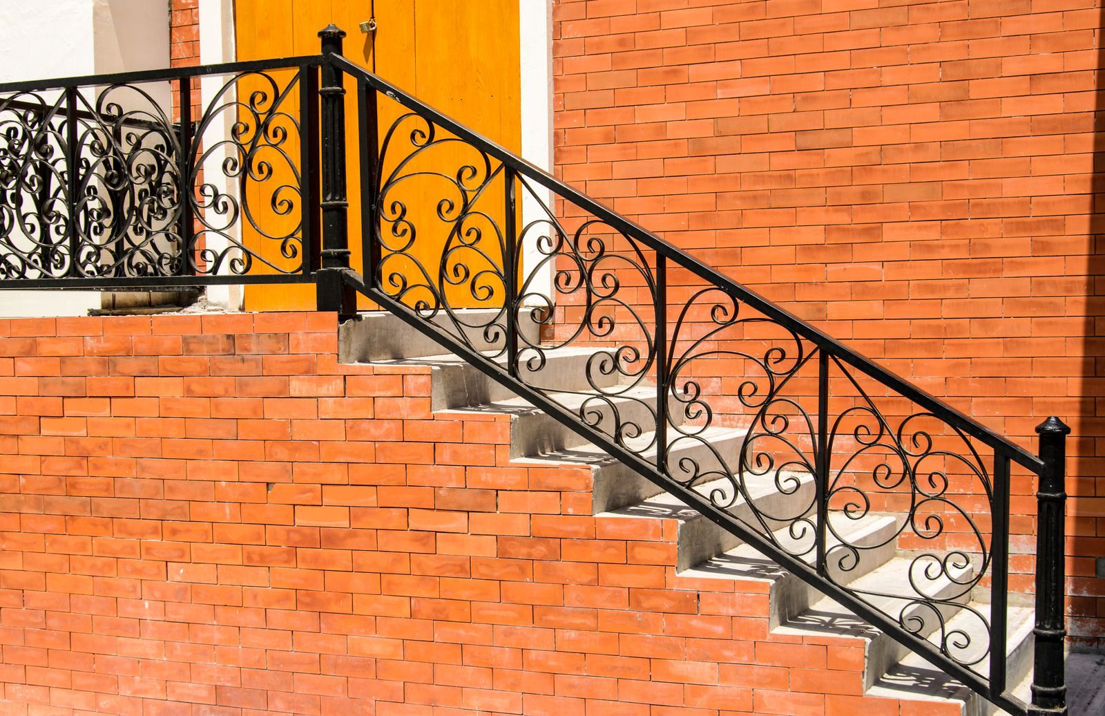 Black wrought iron railing on brick steps leading to a door.