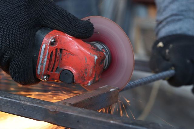 Person in black gloves uses an angle grinder to cut metal, creating sparks.