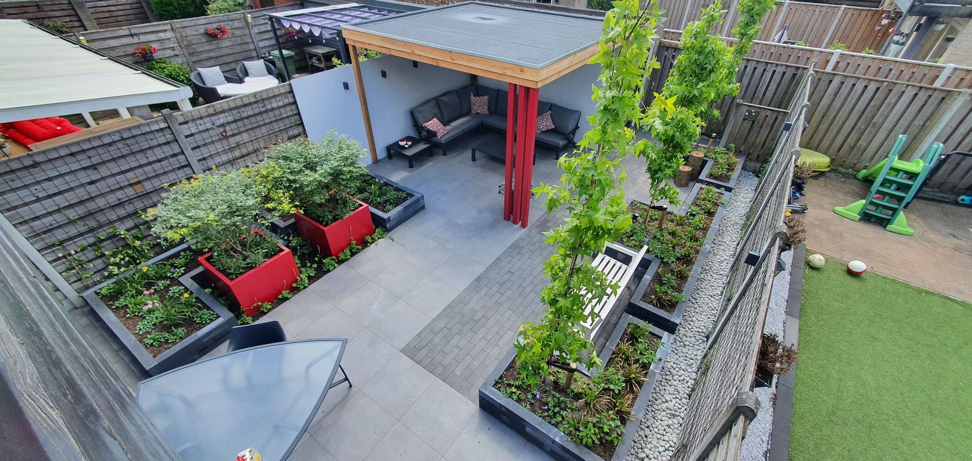 Moderne daktuin met verhoogde plantenbakken, banken en een overdekte zithoek op een stenen terras.