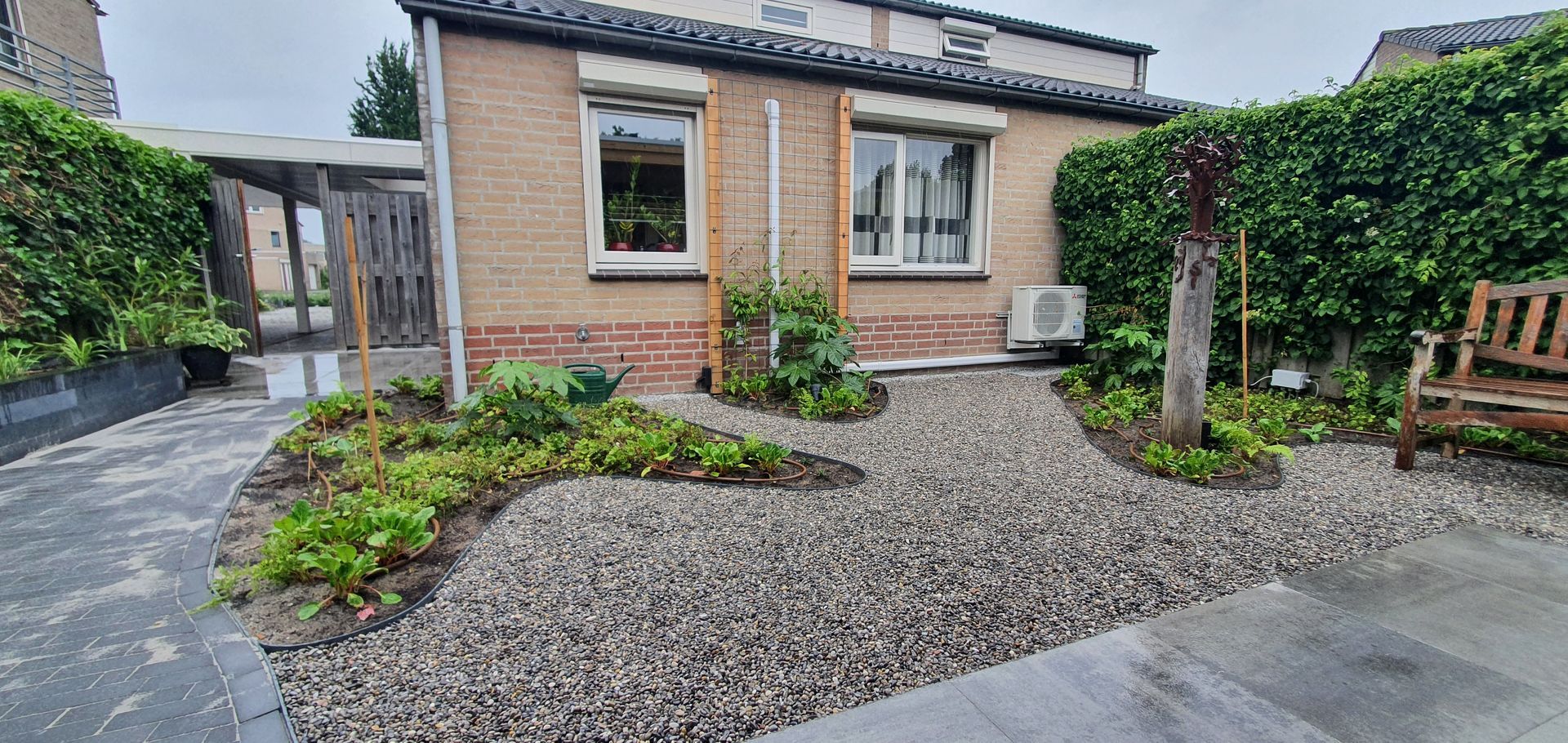 Klein bakstenen huis met grindtuin aan de voorzijde, heg en geplaveide oprit onder een bewolkte hemel.