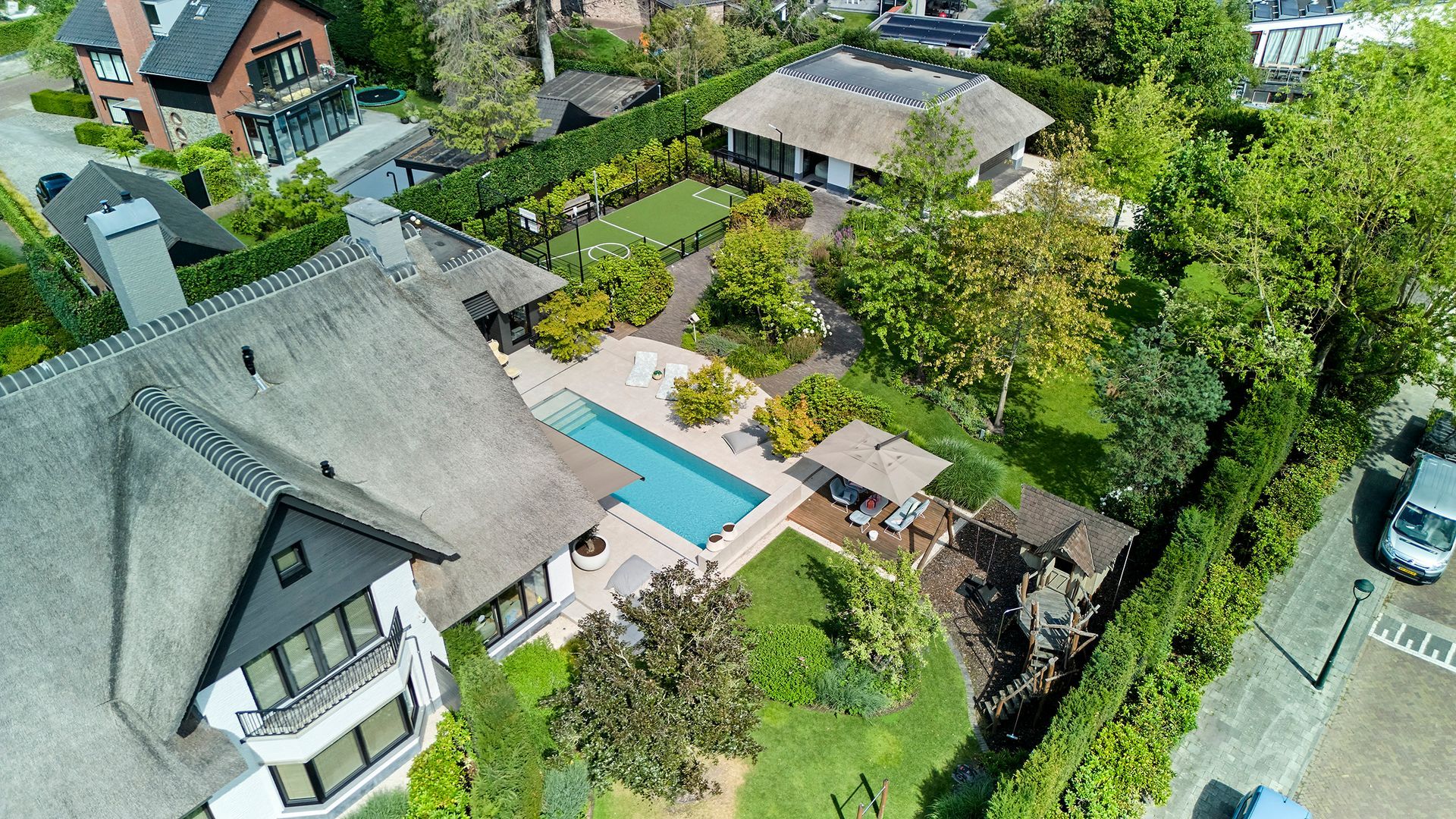 Luchtfoto van een huis met een zwembad, terras en weelderige tuin in de achtertuin, gelegen aan een straat.