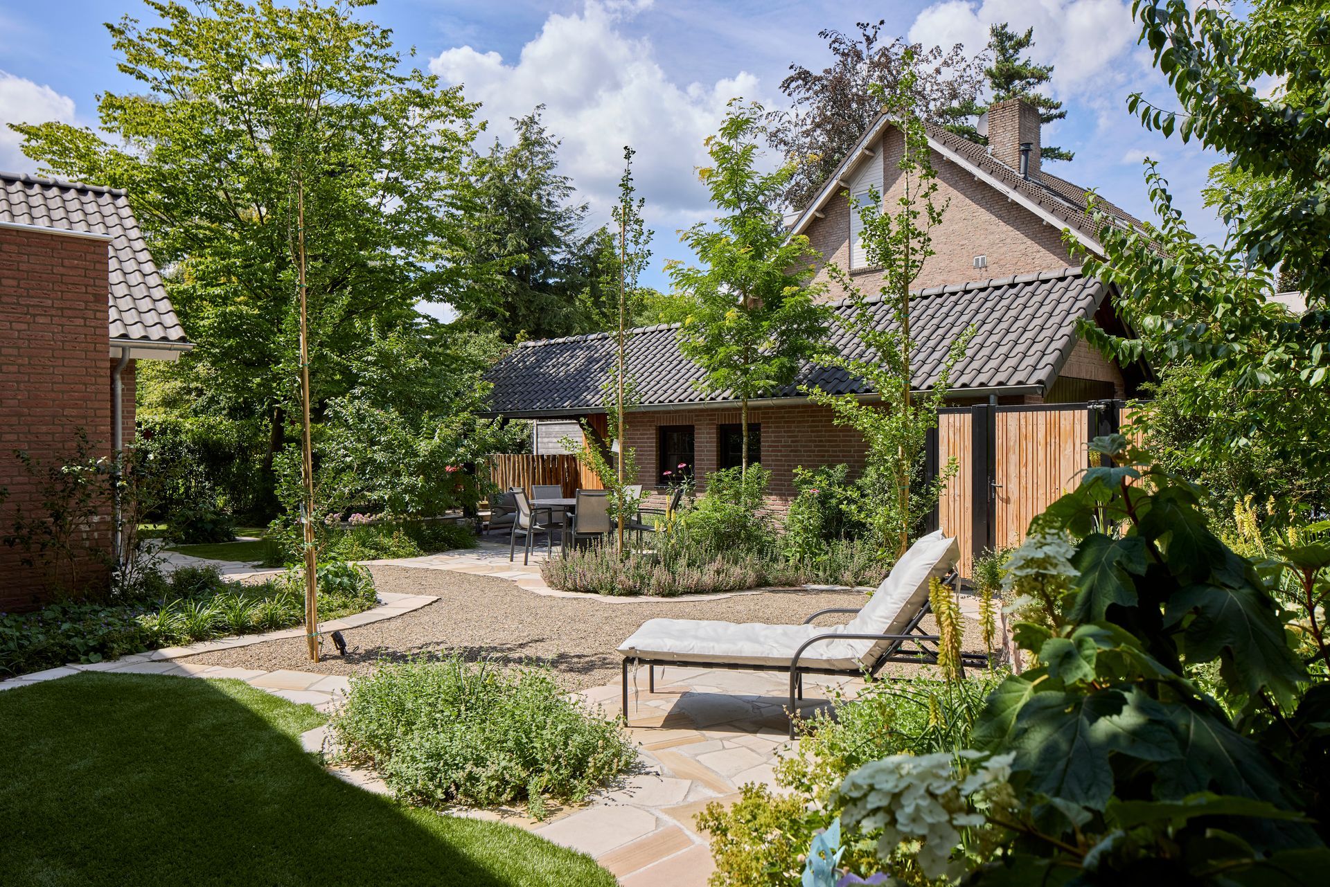 Binnentuin met terrasstoelen, stenen pad en bakstenen huisjes onder een blauwe hemel