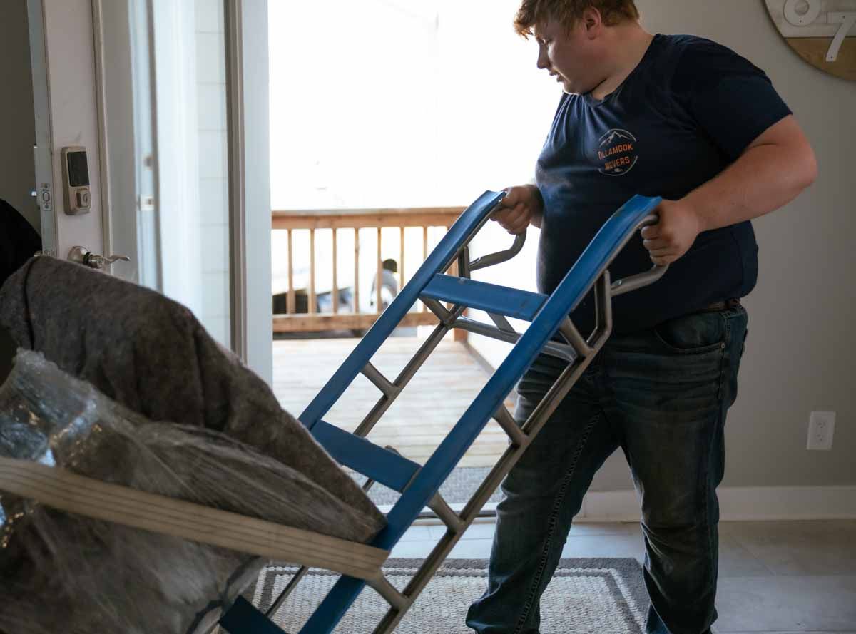 A man is pushing a cart with a chair on it
