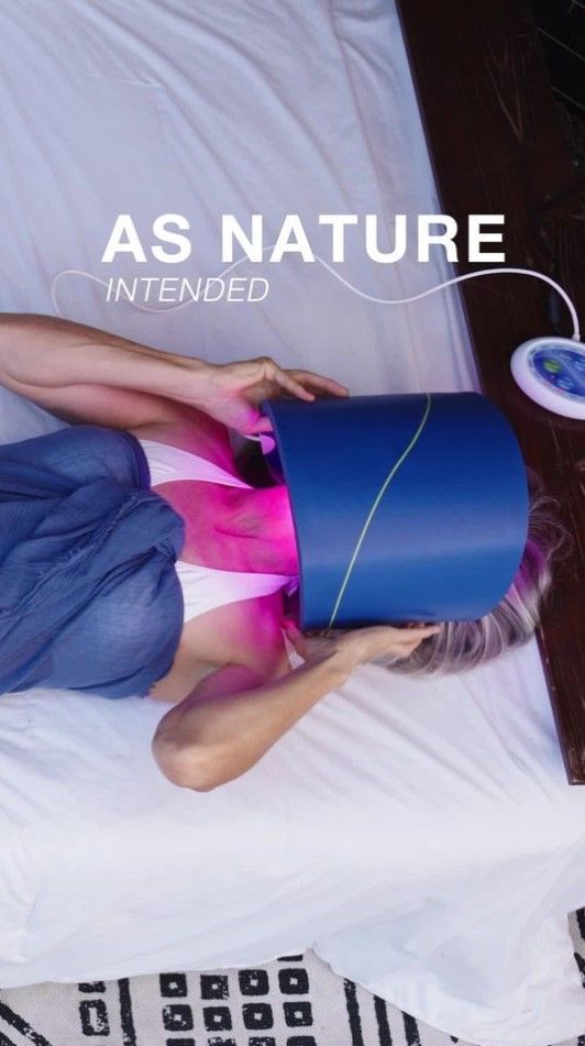 Person lying down with a blue facial mask, pink-lit device, and text “AS NATURE INTENDED” nearby