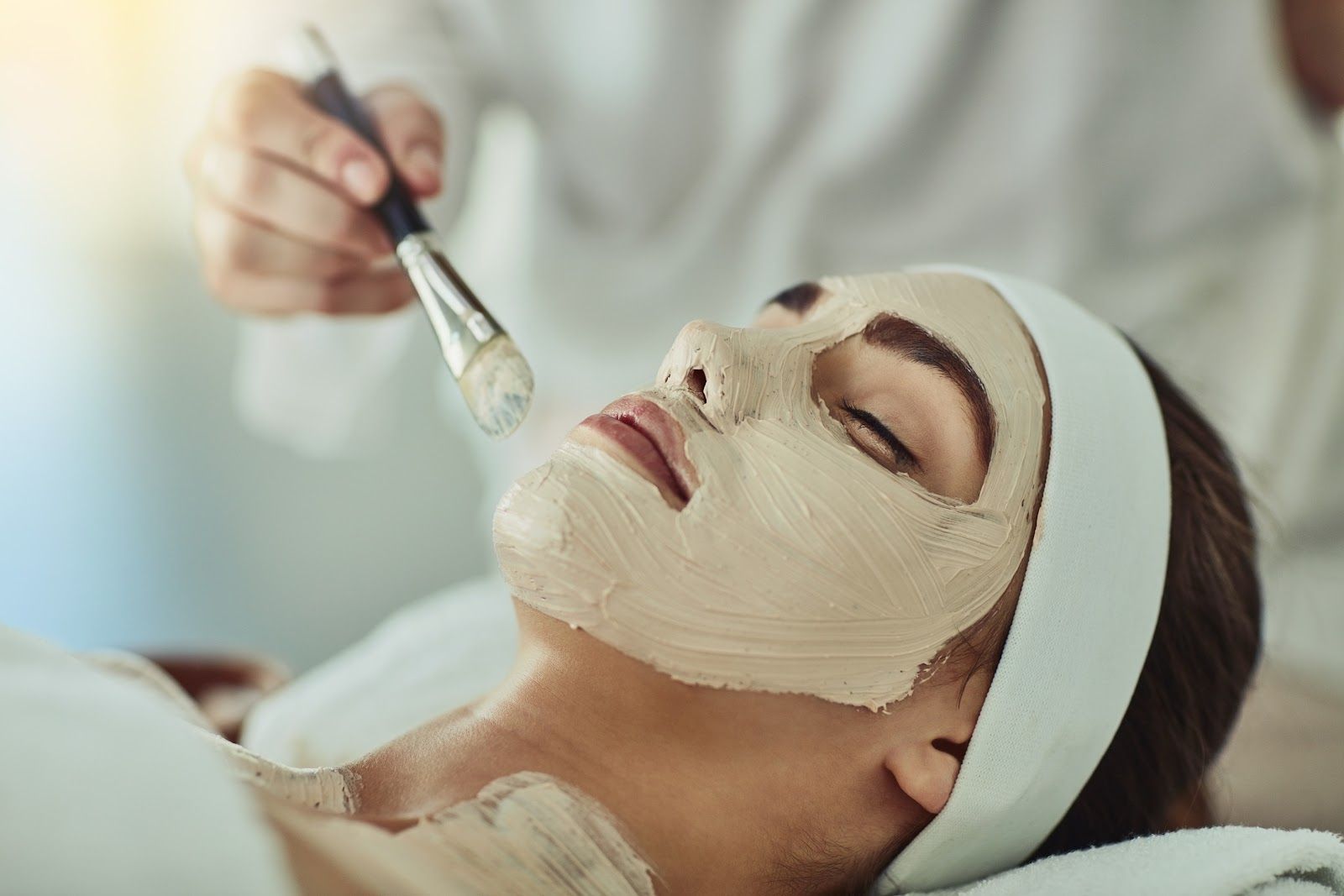 Woman receiving a facial mask application with a brush in a spa setting