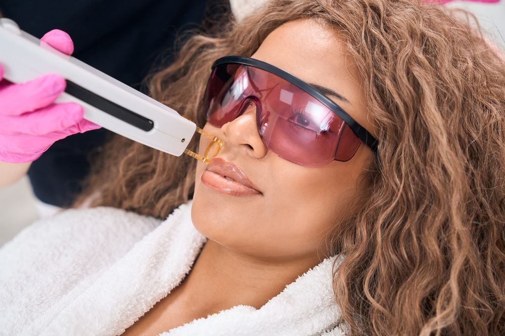 A person wearing protective goggles receives a laser skin treatment on their upper lip from a gloved practitioner.
