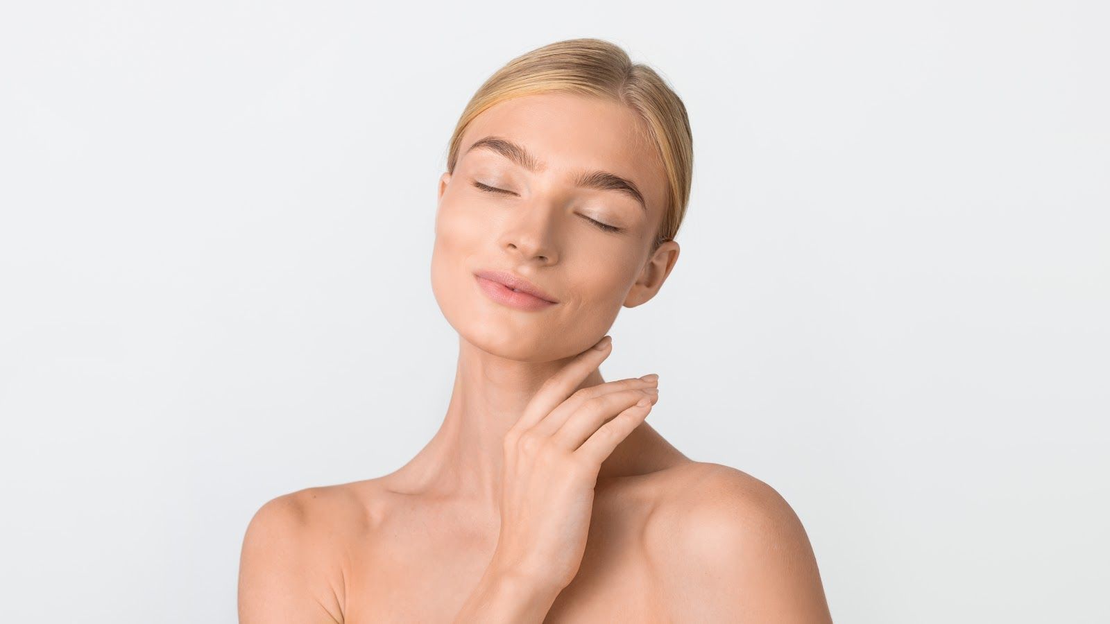 Close-up of a relaxed person with eyes closed, gently touching their neck against a light background.
