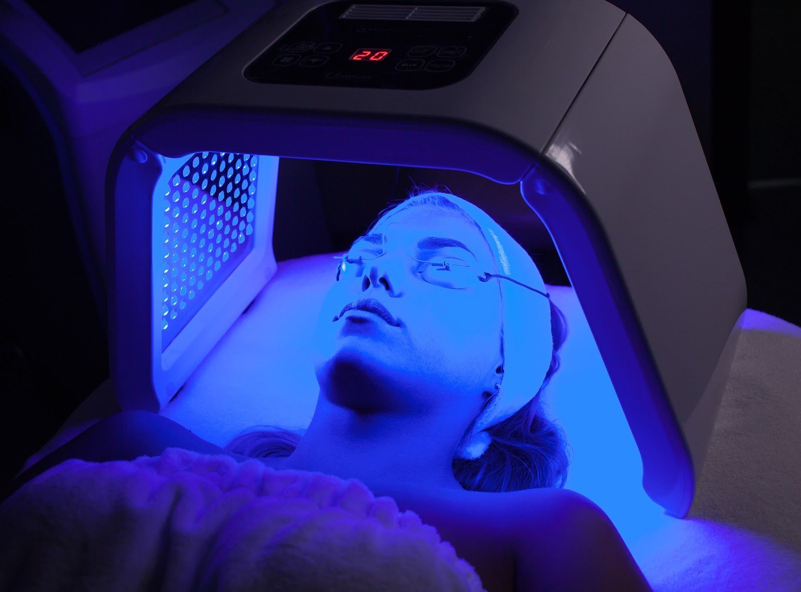 Person lying under a blue LED light therapy mask with a closed-eye, relaxed expression