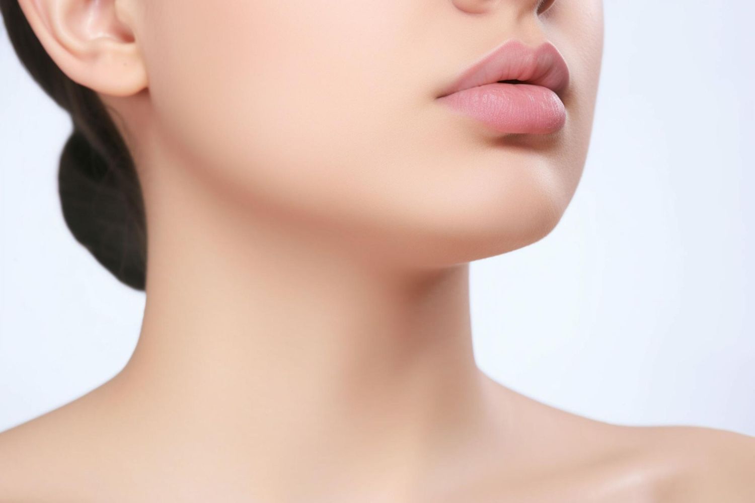A close-up view of a person's lower face, chin, and smooth neck against a plain, light-colored background.