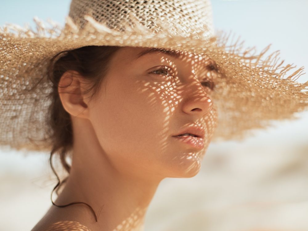 A person wearing a wide-brimmed straw hat casting a dappled grid pattern of shadow across their face.