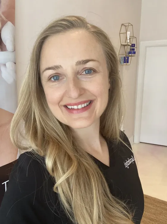 A woman with long blonde hair is smiling and wearing a black shirt.