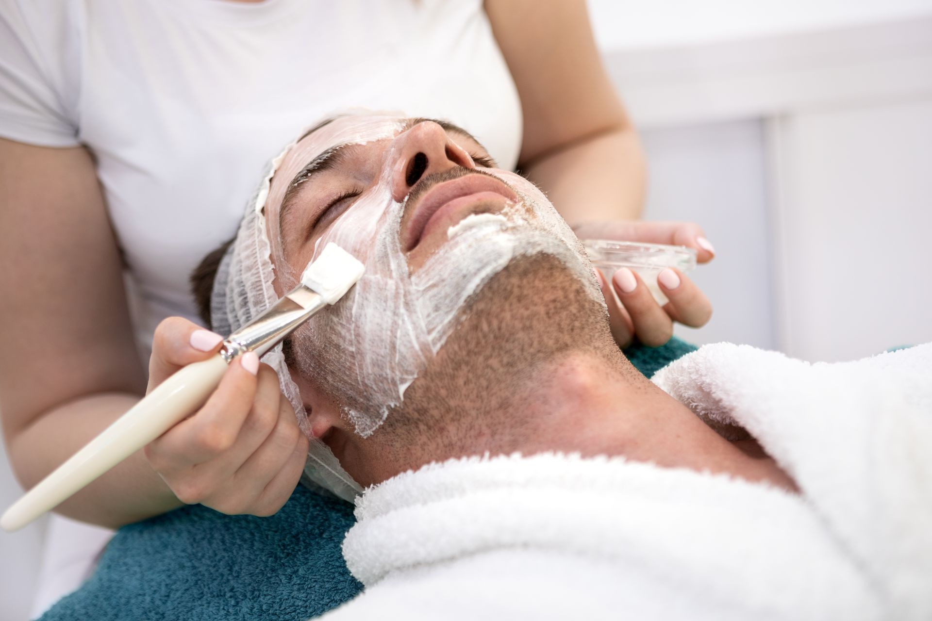 A woman is smiling while applying cream to her face.