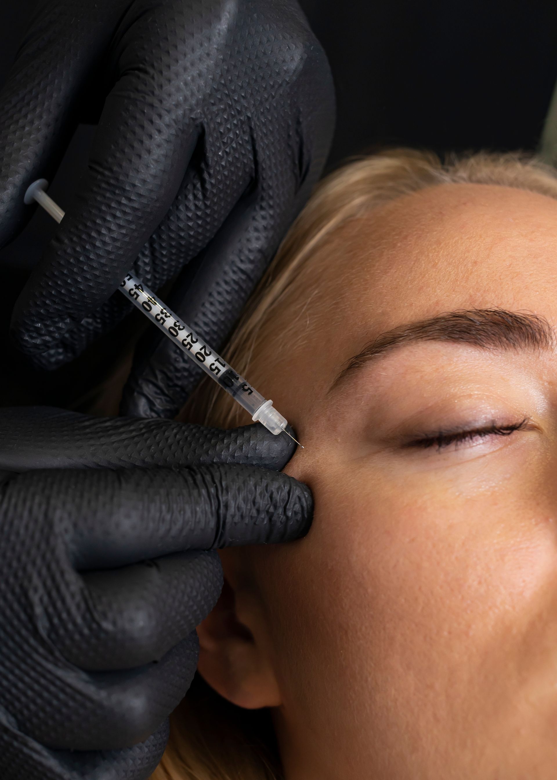 A woman is getting a botox injection in her forehead.