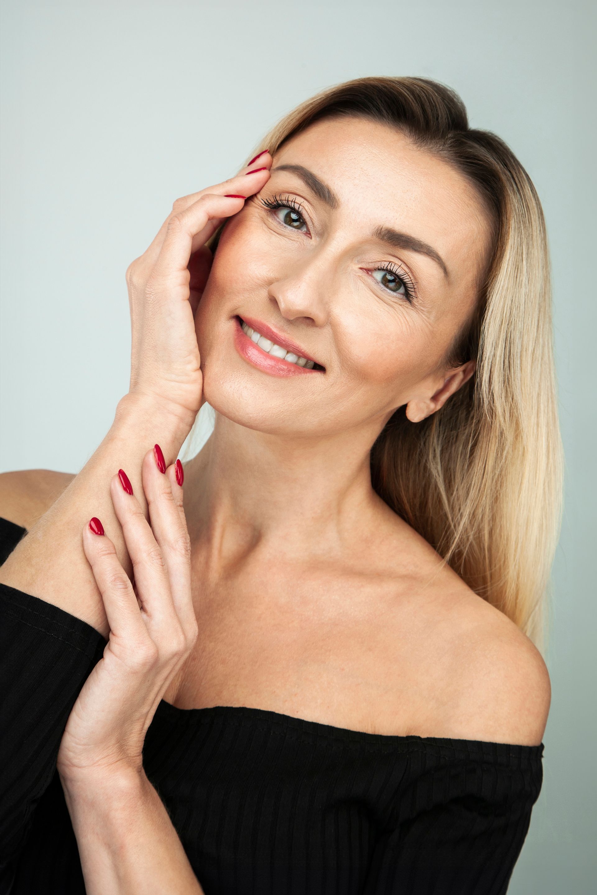 A woman with red nails is smiling and touching her face.