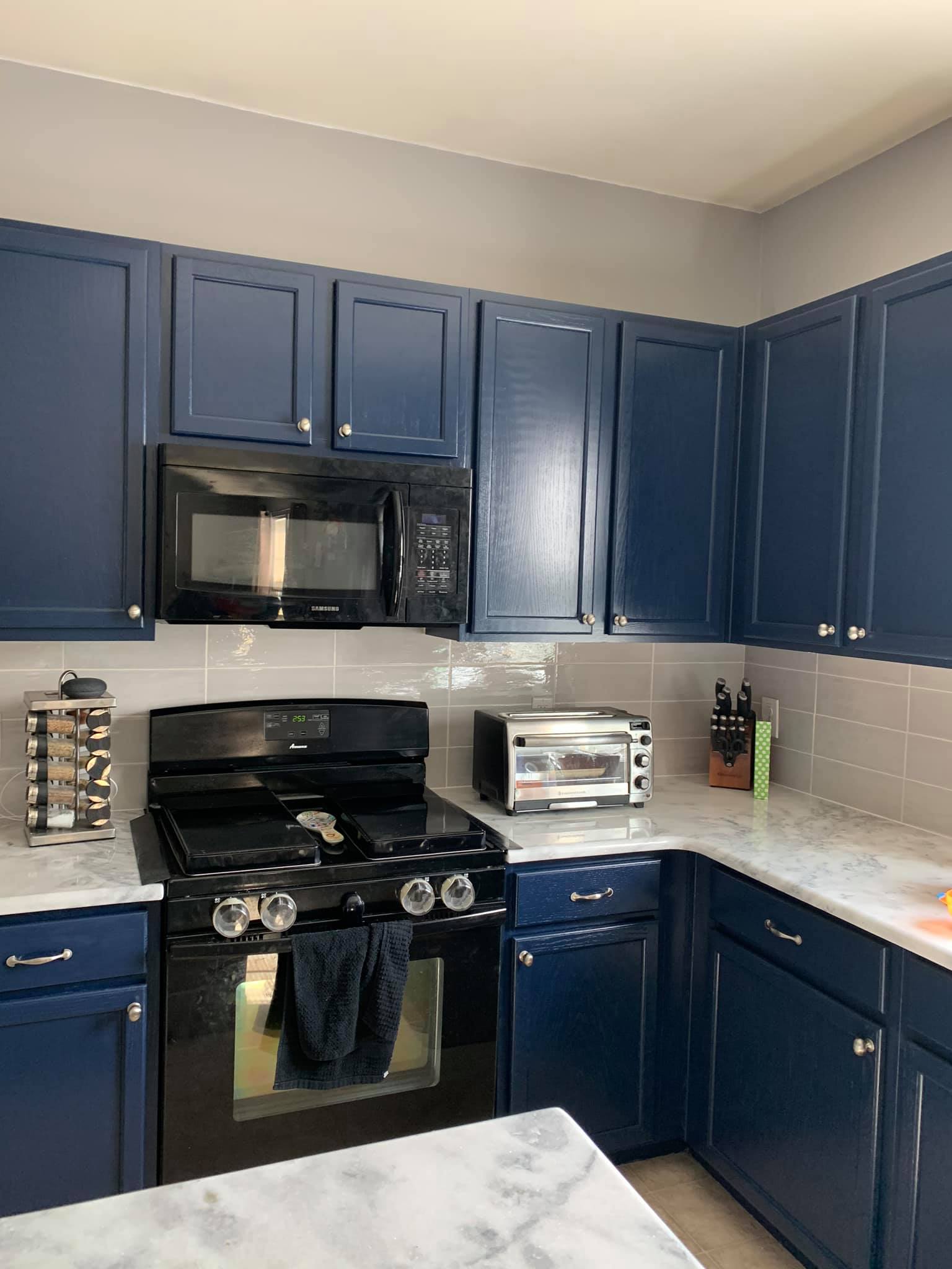 Navy blue kitchen cabinets with a black microwave and stove, white countertops, and gray backsplash.