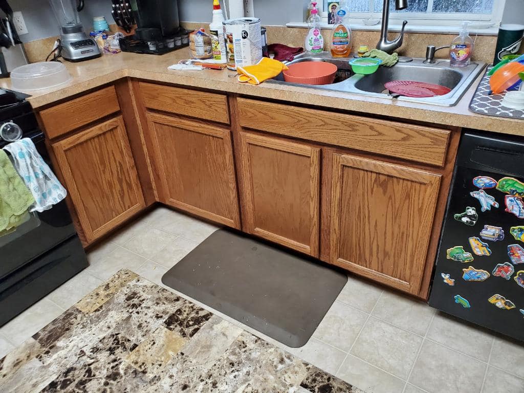 Kitchen with wooden cabinets, sink with dirty dishes, and a patterned rug on the floor.