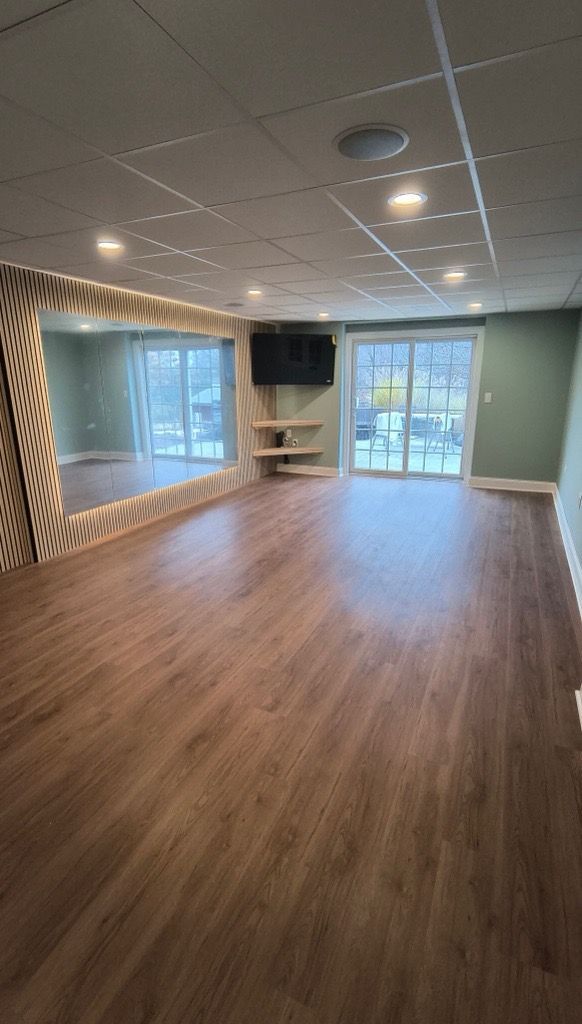 Empty room with wood floors, mirrored wall, TV, and sliding glass doors.