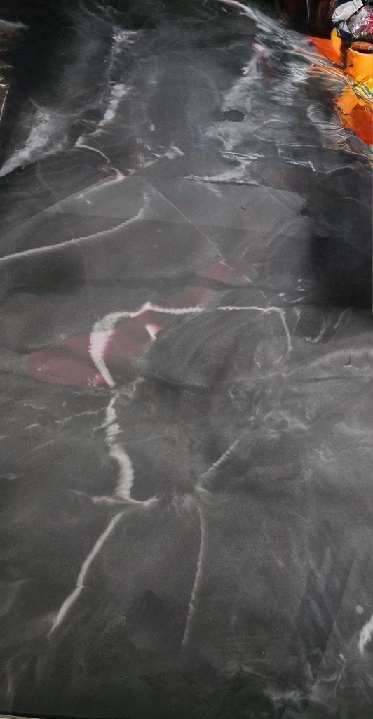 Dark, textured surface with white streaks, possibly marble, orange items visible in corner.